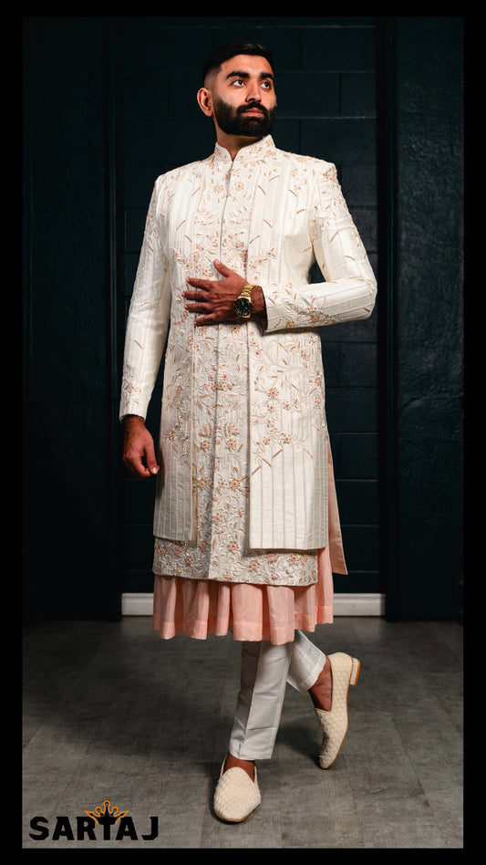Ivory Amir-e-Vastra groom sherwani in Dupion silk, featuring delicate floral embroidery in soft peach threads and refined tonal beadwork, paired with a Dupion Anarkali-style kurta and cotton lycra churidar.